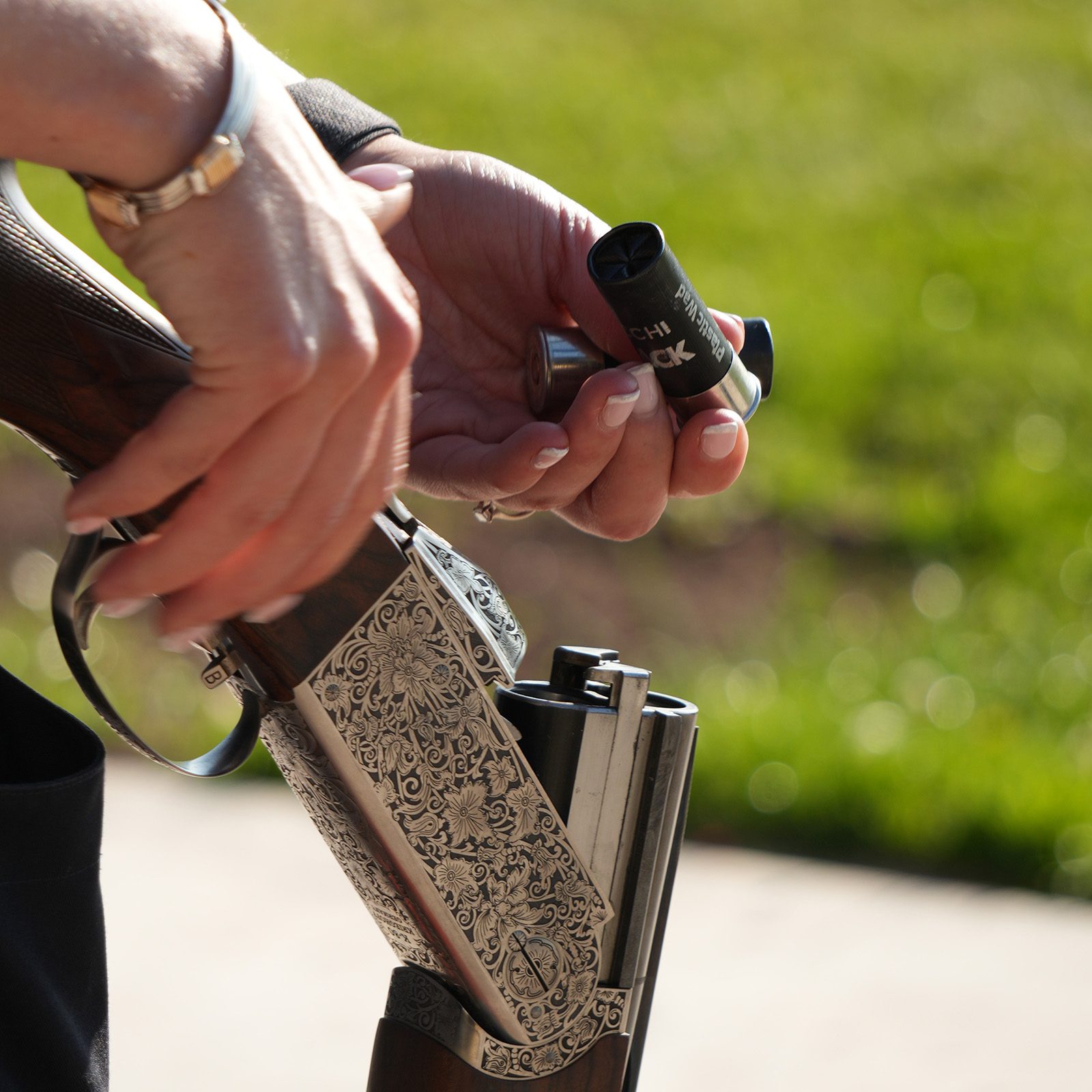 A shooter loading Fiocchi FBlack plastic-wad cartridges into the barrels of an engraved over-and-under shotgun.