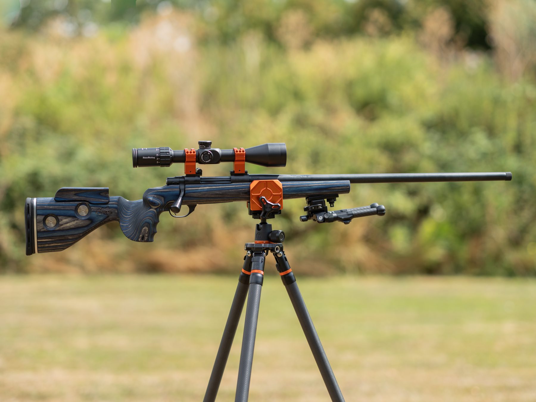 A scoped rifle resting on a 3 Legged Thing tripod on a grass range