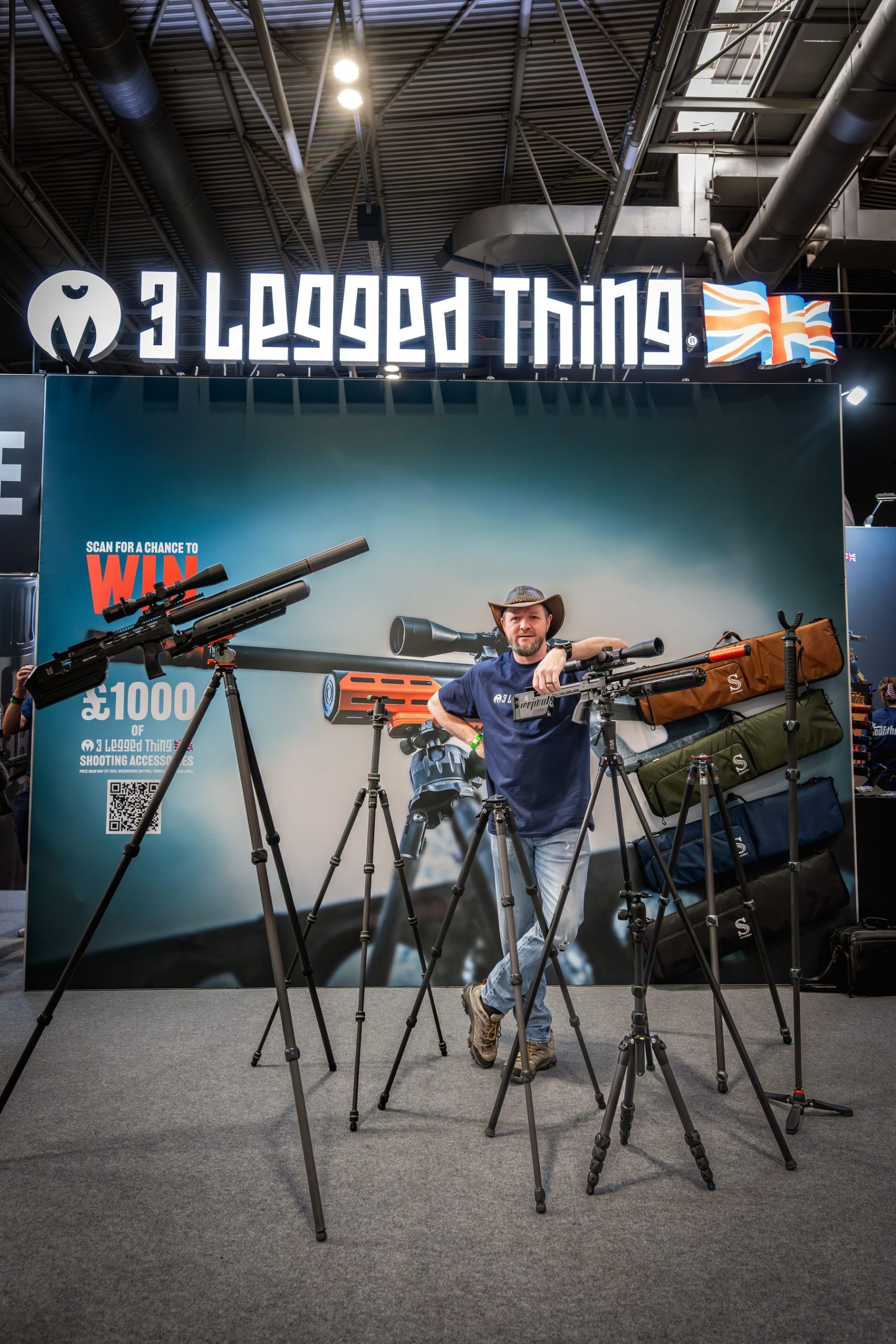 Danny Lenihan holding a rifle on a 3 Legged Thing tripod in front of the company's branded stand at the NEC