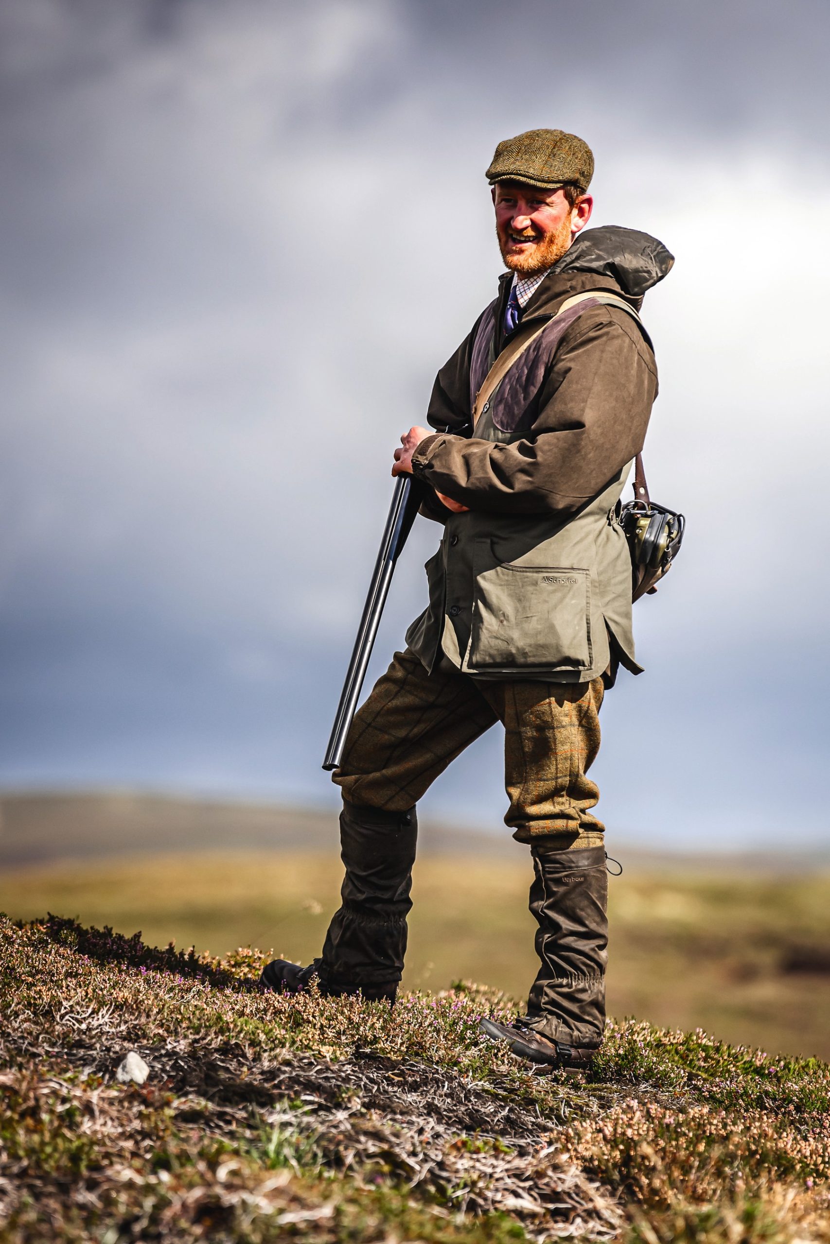 A Gun standing on open moorland with a shotgun broken over his arm