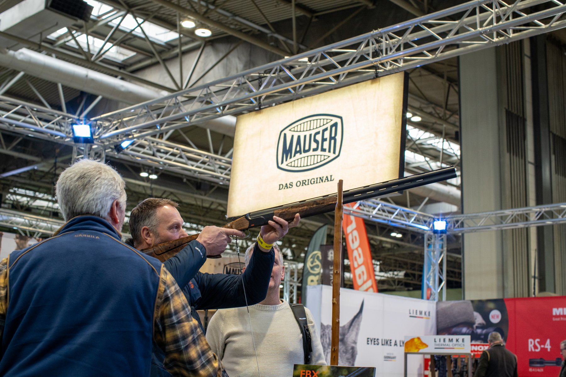 A visitor shouldering a rifle beneath the Mauser sign on the Blaser Group stand