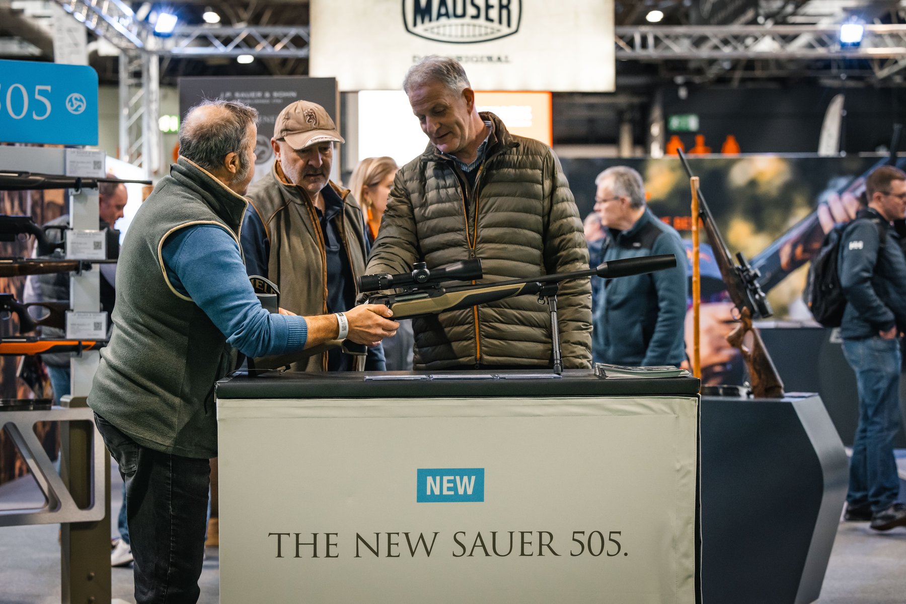 Visitors handling a new Sauer 505 rifle on the Blaser Group stand beneath the Mauser sign