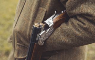 A shooter in traditional clothing holding a broken shotgun over the forearm