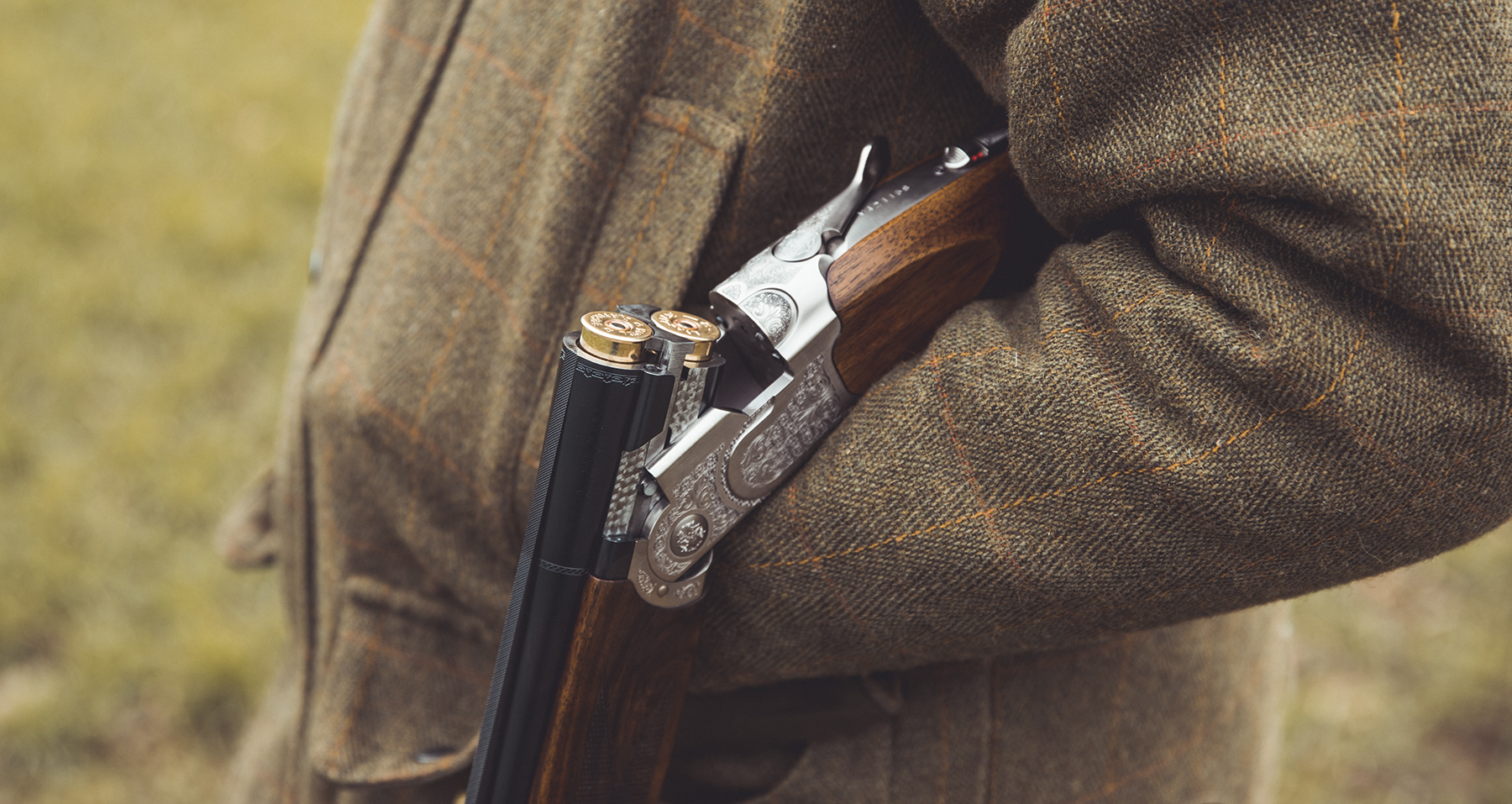 A shooter in traditional clothing holding a broken shotgun over the forearm